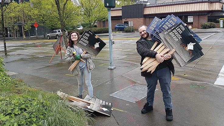 Two campaigners for better plastics reporting by Amazon carry yard signs.