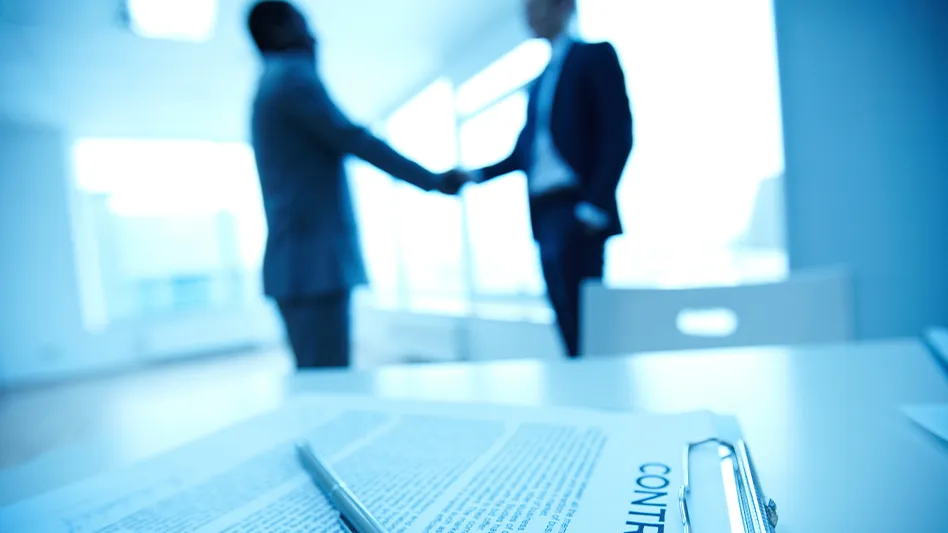 two businessmen shaking hands in the background, with a contract on a table in the foreground