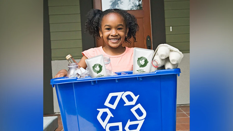 A girl holds up a blue recycling bin containing recyclable plastic items.