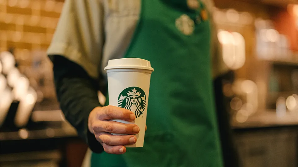 A Starbucks employee holds a white cup of the company's coffee.