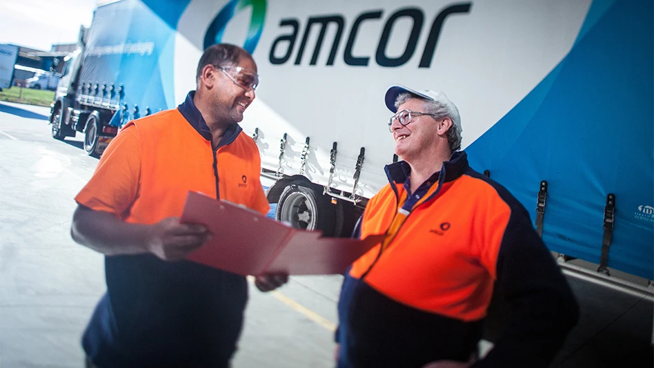 Two Amcor workers talk to each other in front of a large Amcor truck.