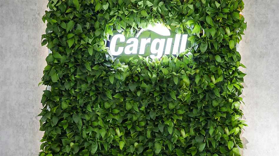 The Cargill logo, illuminated amongst a wall of green plants.