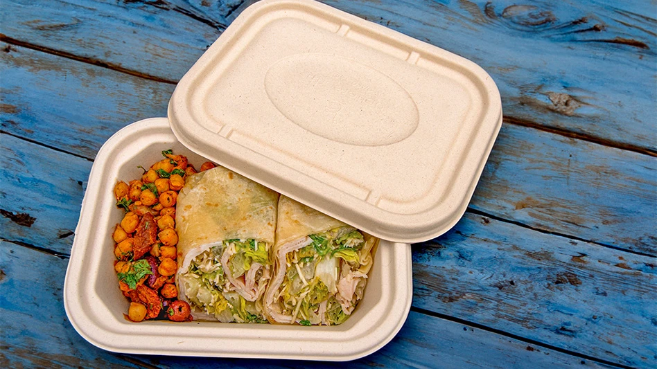 A Better Earth rectangular fiber container with food inside of it, sitting on a blue picnic table.