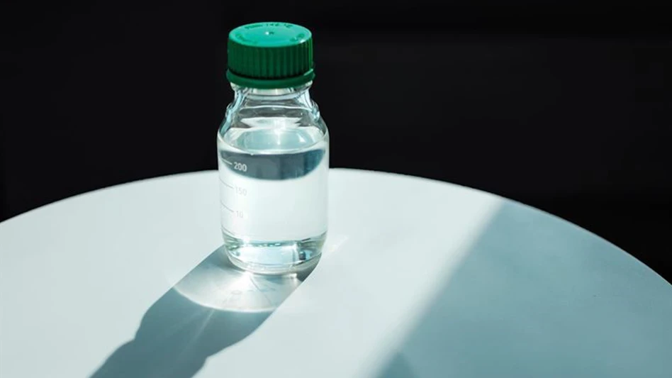 A bottle of Neste RE sits atop a white table, with a black background.