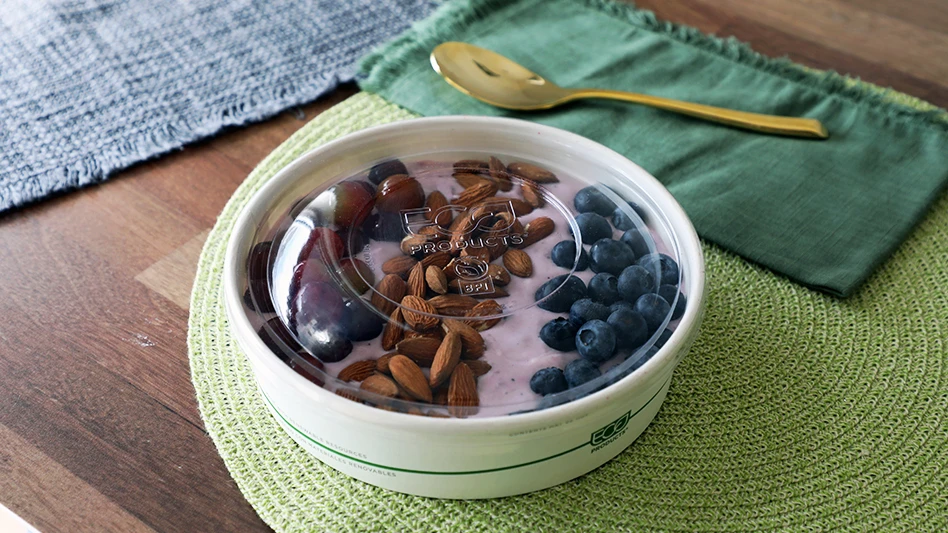 bowl with purple yogurt, berries and almonds, on a wooded table with a green placemat and napkin