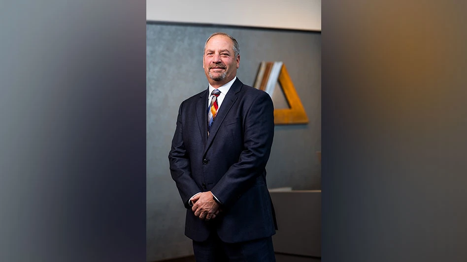 a man wearing a gray suit and tie smiles in front of the Alter logo