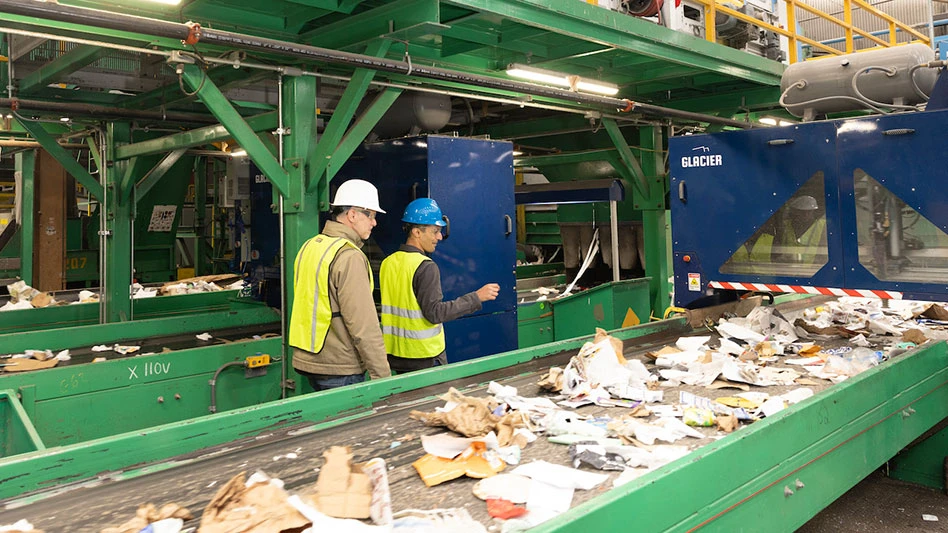 two men walk by a conveyor belt covered with recyclables and a Glacier robot