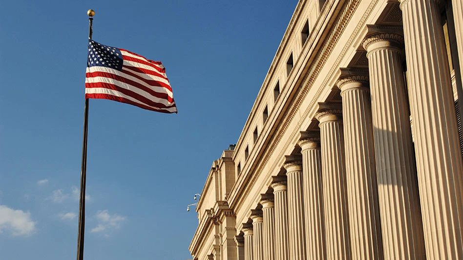 us flag against a blue sky with a government building to the right