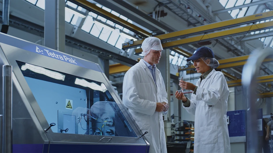 Two workers stand next to a Tetra Pak homogenizer made with Outokumpu stainless steel.