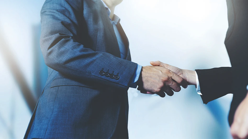 Two businesspeople shaking hands with a building in the background.