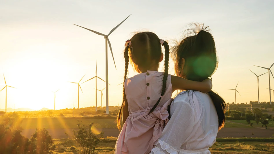 A woman holds a toddler as they watch windmills spin at sunset.