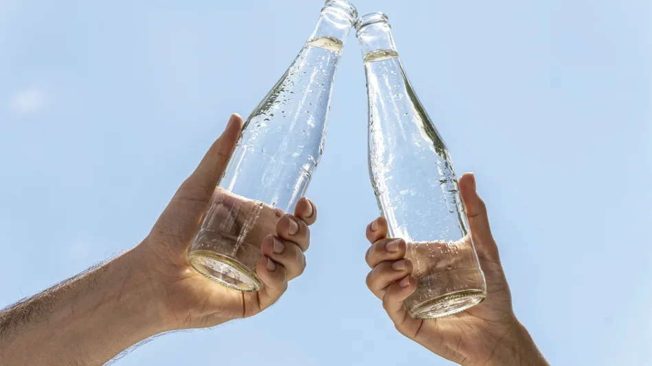 Two hands hold up clear glass bottles.