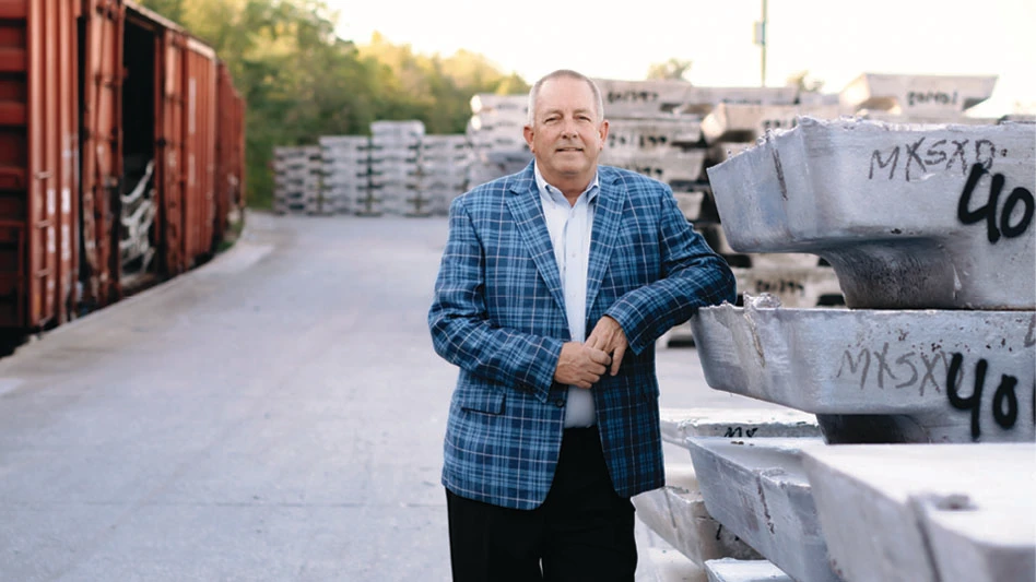 Owl's Head Alloys President Michael Boyle in a checkered blue jacket leans on some aluminum ingots