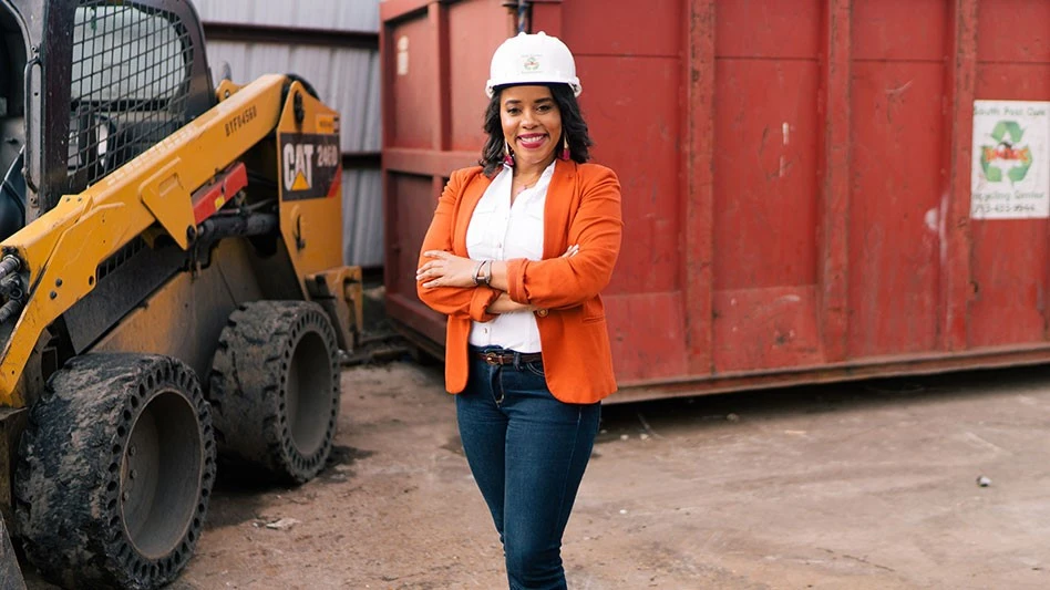 a woman stands in front of skid steer and an industrial container