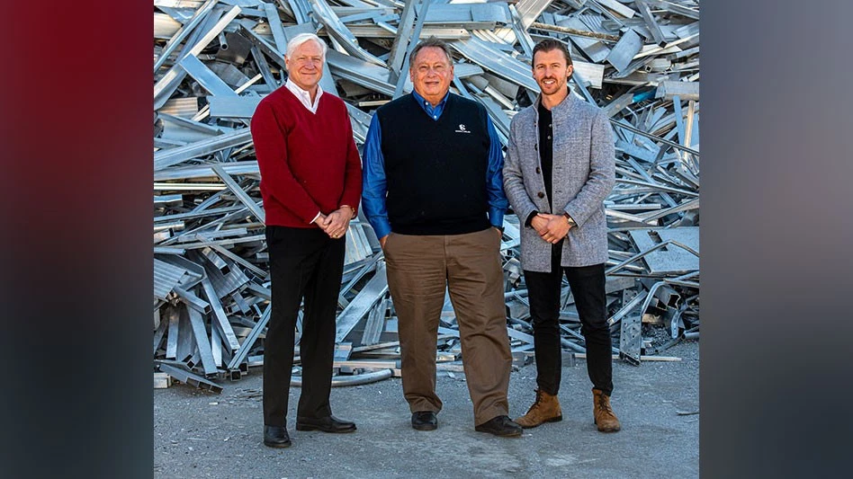 three men stand before a pile of aluminum scrap